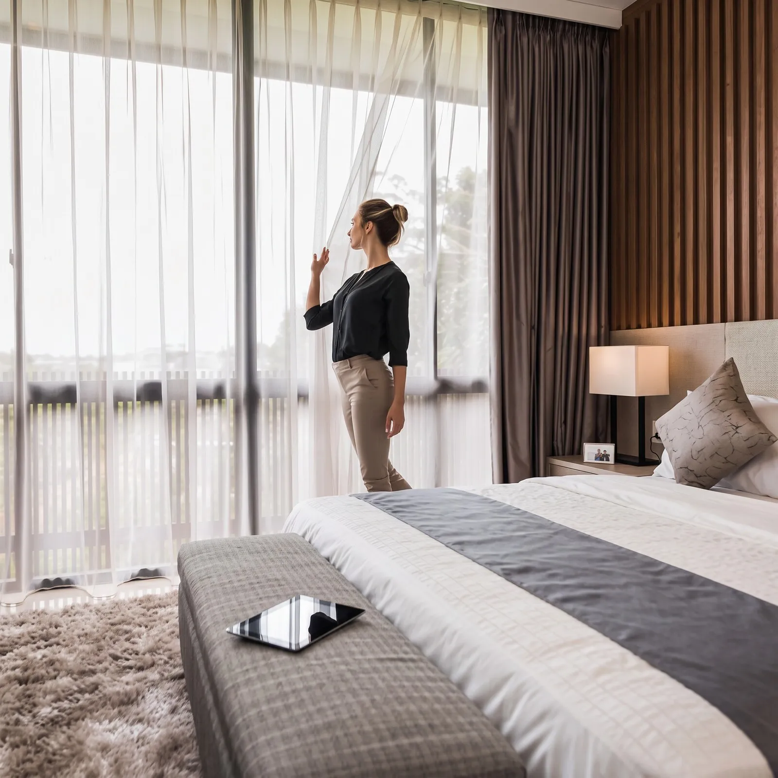 Quarto com cama, cortinas claras e vista pela janela
