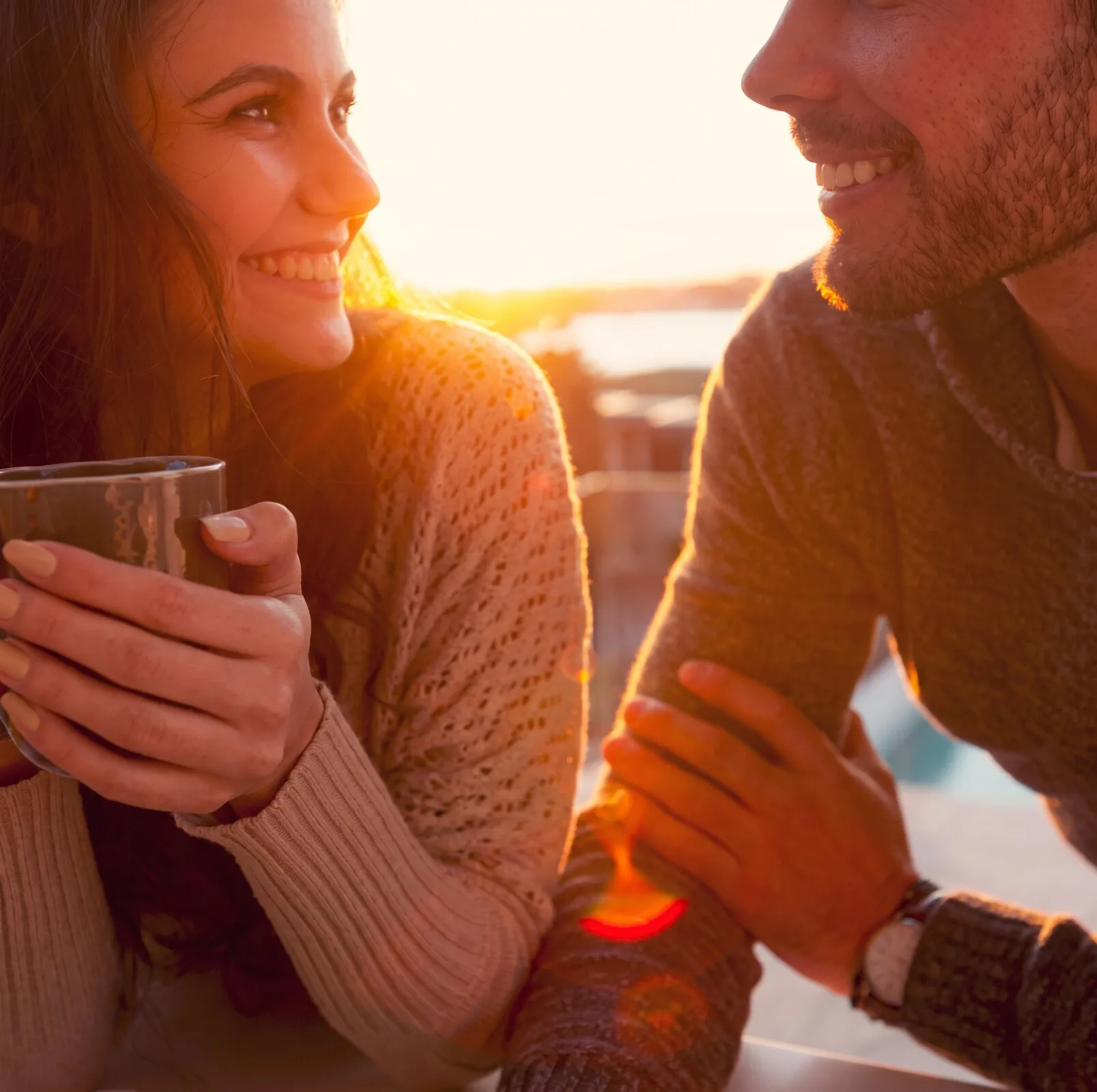 Casal sorrindo enquanto toma café ao ar livre no fim de tarde